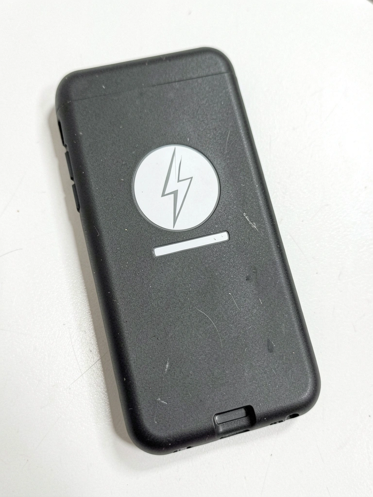 Carregador magnético branco acoplado à parte traseira de um iPhone sobre mesa de madeira clara.