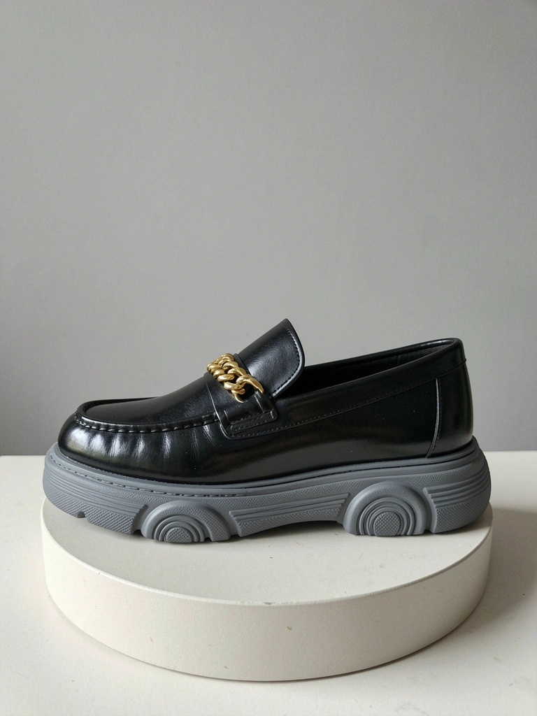 Mocassim de couro preto brilhante sobre superfície clara, visto de cima.