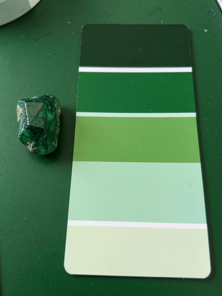 Amostras de pedra berilo verde e cartelas de tinta em degradê sobre superfície clara.